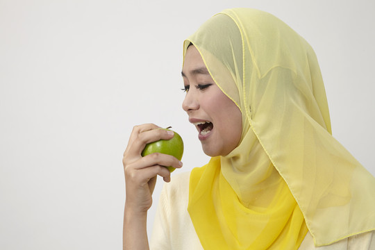 一个马来女人手里拿着青苹果，在家里。健康饮食理念。