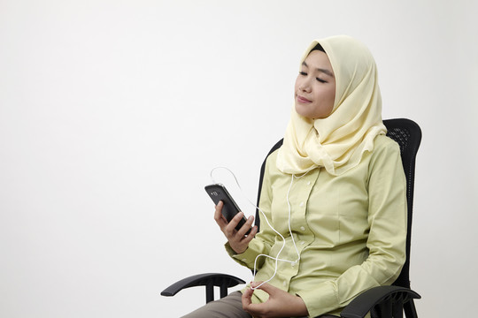 马来妇女坐在办公椅上听音乐