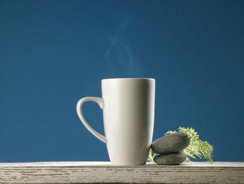 一杯热咖啡，蓝色背景，桌上有装饰石