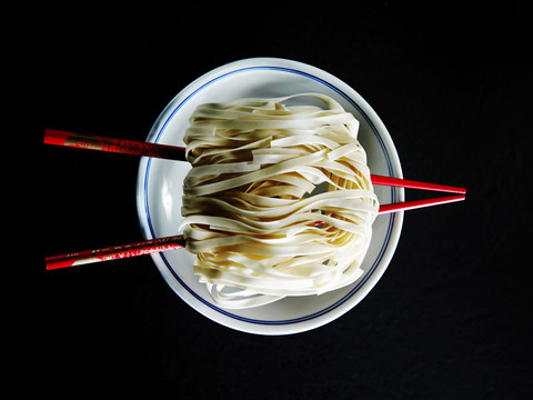 一双红色的筷子，放在碗上，筷子上有粉丝