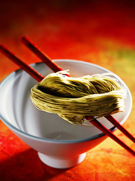 一双红筷子放在一个白碗上，上面有粉丝