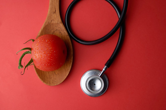 顶视图红色番茄和听诊器在一个木勺上隔离在红色背景上