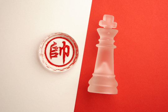 中国象棋（翻译：将军或国王）和国际象棋国王-红色背景上的玻璃棋