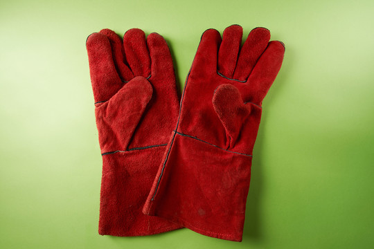 一双红色的皮革工作手套，隔离在绿色背景上。