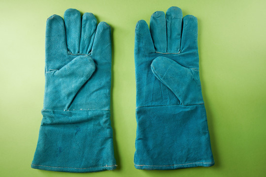 在绿色背景上隔离的一对蓝色皮革工作手套。