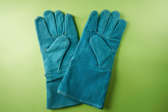 在绿色背景上隔离的一对蓝色皮革工作手套。