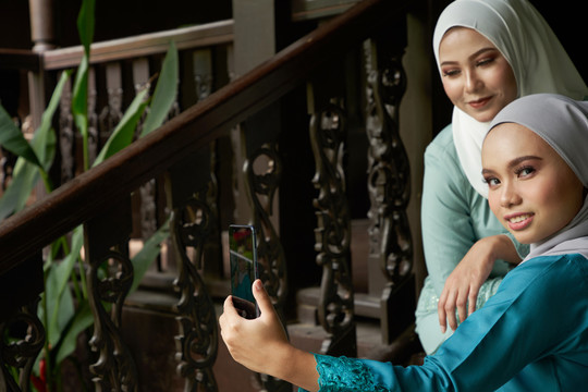 戴头巾的亚洲穆斯林妇女在传统的马来人家里用智能手机自拍