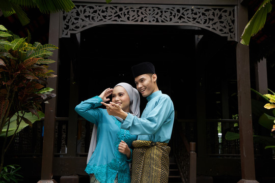 穿着传统服装的马来夫妇站在传统的房子前