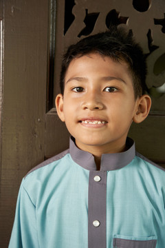 在开斋节或哈里拉亚节庆祝活动期间，马来男孩的肖像画以马来传统布料为背景，以木制的渴望为背景。