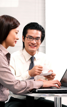 一个戴黑框眼镜的男人在观察一个正在用笔记本电脑工作的女人
