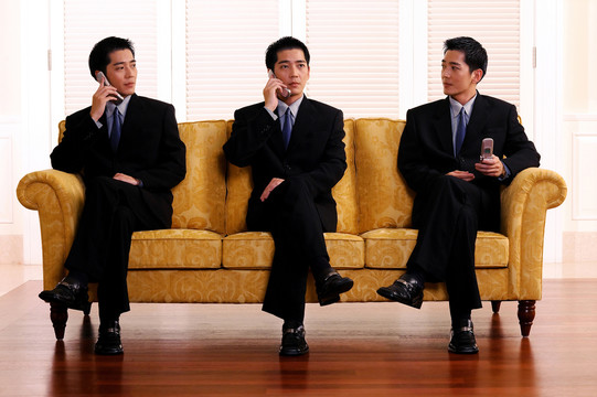 三个一模一样的男人坐在黄色沙发上拿着手机