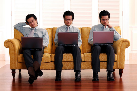 三个一模一样的男人坐在黄色沙发上，笔记本电脑放在他们的笔记本上