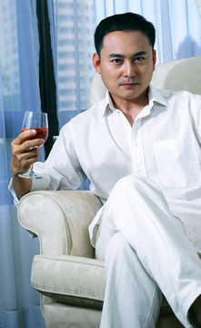 一个男人拿着一杯红酒在沙发上摆姿势