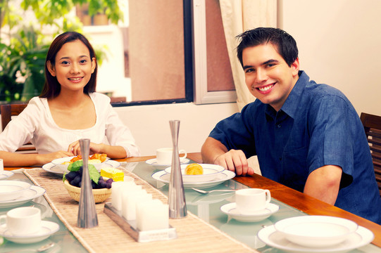 一对夫妇在餐桌边吃饭，对着镜头微笑