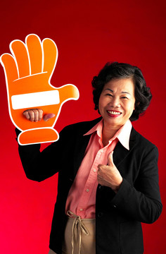 摄影棚拍摄的一位老妇人举着一只纸板手竖起大拇指