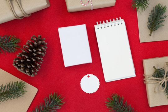 圣诞和新年快乐构图的俯视图、礼品盒、松果、红色背景上的冷杉枝以及文本的复制空间白皮书