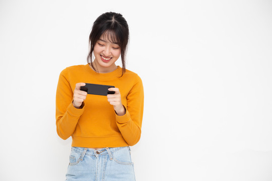 在白色背景下，亚洲青少年玩家在手机上微笑和玩在线游戏