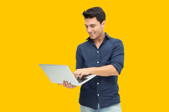 一个兴奋的男人的肖像，拿着笔记本电脑，孤立在黄色背景上，感觉幸福，白人男性模特