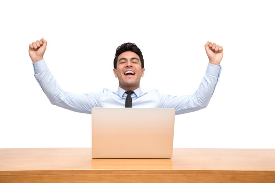 兴奋的英俊商人感觉赢家庆祝胜利在线商业成功，坐在桌子上，笔记本电脑被隔离在白色背景上