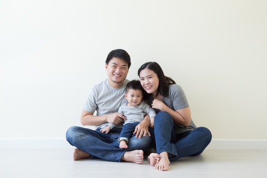 微笑的亚洲夫妇和儿子坐在房间的地板上，快乐的泰国和中国血统的家庭观念