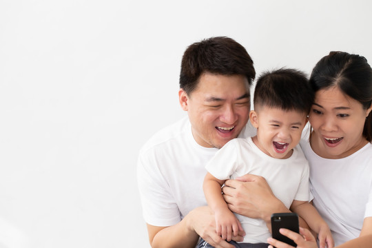 快乐的年轻亚洲家庭，儿子在智能手机上看有趣的视频，有孩子的父母喜欢玩游戏或使用移动应用程序娱乐