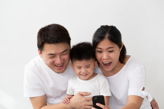 一个快乐的亚洲家庭，儿子在自拍，手机在白色背景下对着镜头微笑
