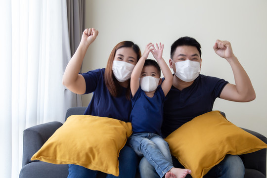 亚洲家庭戴2019冠状病毒疾病预防罩，并在客厅里一起坐在一起。保护家庭免受空气污染概念