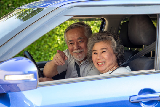 亚洲资深夫妇开车，开心地笑着，带着快乐的积极表情，在驾车旅行的过程中，人们享受着欢笑的公路交通出行理