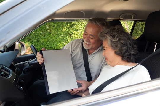 快乐的亚洲老年夫妇坐在车里，手里拿着保险文件