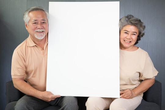 一对亚洲老年夫妇坐在沙发上，手里拿着白色的空白海报