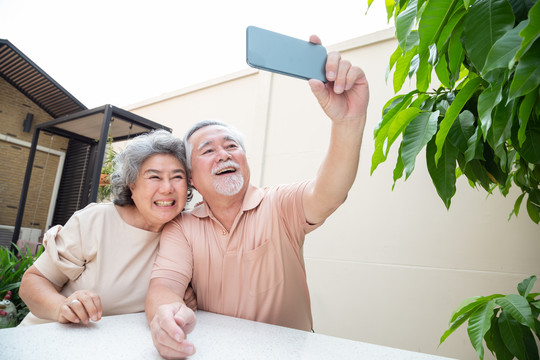 亚洲老年夫妇通过手机视频通话聊天或自拍，老年智能技术和在线行动保持联系的概念