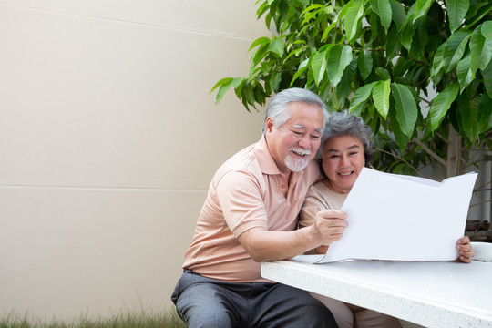 快乐的亚洲成年夫妇在前花园家看报纸或杂志