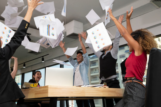 在初创公司合作办公室庆祝成功的同时，一组业务团队举起双臂，投掷文件并取得胜利