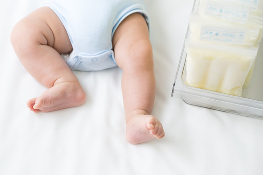 储存袋中冷冻的母乳和躺在白色床上的腿部婴儿