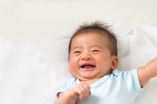 快乐的亚洲小宝宝躺在白色的床上微笑着