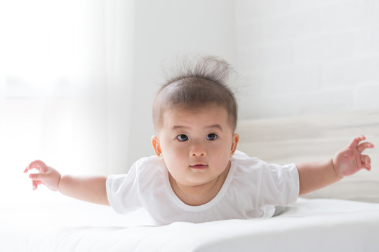 在白色卧室里，一个倒立在床上的亚洲男婴