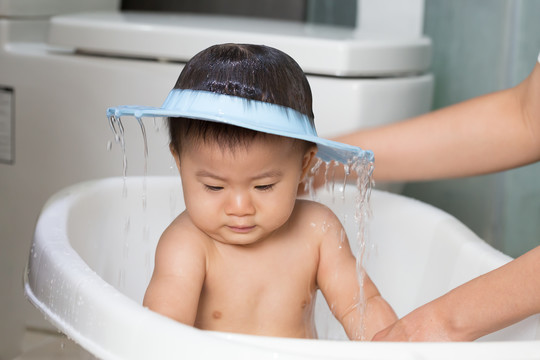亚洲男婴正在妈妈旁边洗澡，戴着淋浴帽。幼儿卫生及护理概念