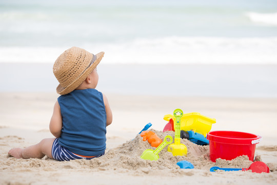 亚洲男婴在沙滩上玩沙子，婴儿1岁