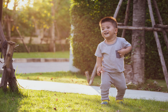 晚上，亚洲男婴在花园里奔跑，阳光从孩子的背上照射下来