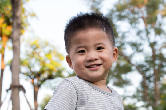 小亚洲男孩站在公共绿地背景上，开心地微笑着。一岁五个月大