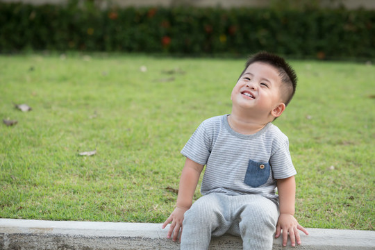 微笑的亚洲男婴坐在公园人行道边上的肖像。快乐有趣的笑脸村花园里可爱可爱的小儿子