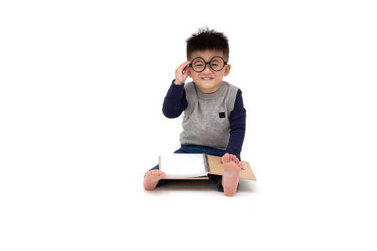 一个可爱的亚洲小男孩戴着眼镜，阅读一本白色背景下的书