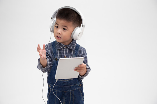 一个心满意足的可爱小孩的肖像，手持平板电脑，在应用程序上听音乐，背景为白色