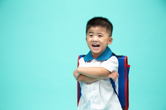 快乐微笑的亚洲小男孩，穿着校服，背着背包，在绿色的背景下享受着孤独的乐趣，幼儿园的第一天和返校的概念