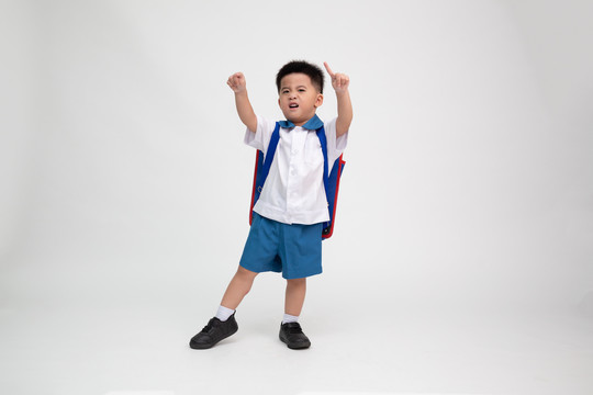 穿着学生制服的亚洲小男孩，背着白色背景的背包，在幼儿园的第一天和回到学校的概念，泰国男孩模型
