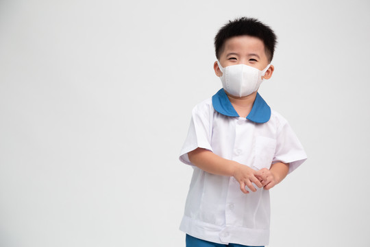 亚洲小男孩穿着学生制服，戴着口罩保护白色背景上分离出的冠状病毒，幼儿园第一天和返校概念，泰国男孩模型