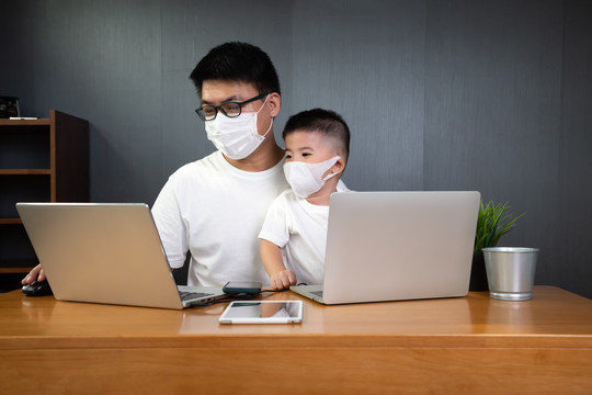 支持2019冠状病毒疾病的亚洲男子IT支持，在电脑笔记本电脑上与儿子一起远程桌面，戴防护性防护面具，