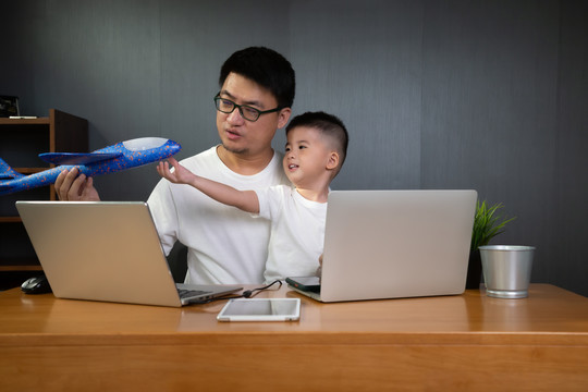 亚洲男子it支持与儿子在笔记本电脑和远程桌面上工作。在家工作的概念