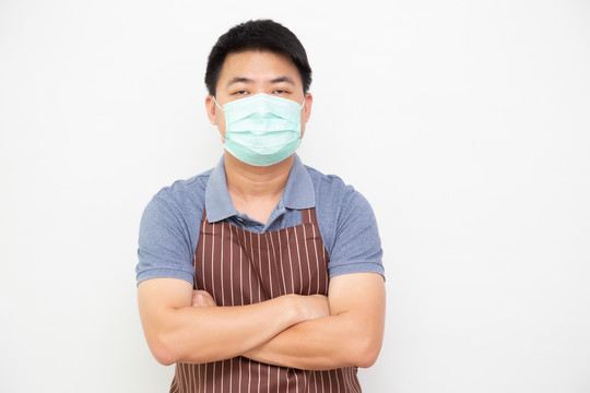 亚洲工人鲜活市场的肖像，棕色围裙，戴着预防病毒的医用防护面具，双臂交叉，孤立地站在白色背景上
