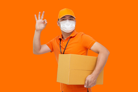 送货员持2019冠状病毒疾病防护罩，戴上防护罩，防止橙色背景、网上购物和快速快递服务